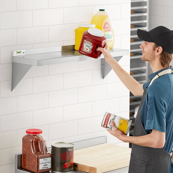 A man's hand holding a plastic container of food on a Regency stainless steel wall shelf.