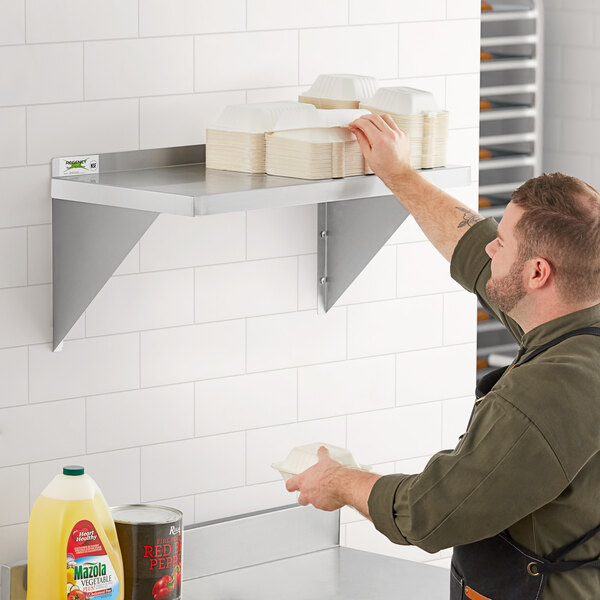 A man in a black shirt putting plates on a Regency stainless steel wall shelf.