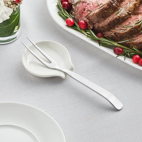 An Acopa stainless steel 2-tine serving fork on a plate with meat and herbs.