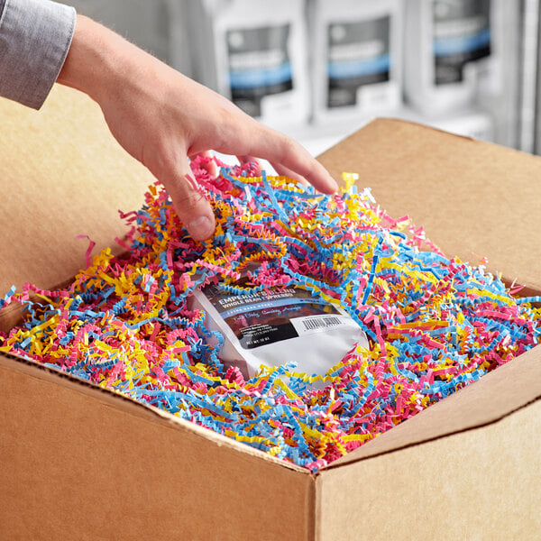A hand reaching out to a box with colorful shredded paper.
