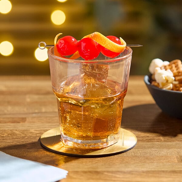 An Acopa Memphis old fashioned glass filled with a drink, ice, and fruit on a wooden table with a bowl of popcorn and nuts.