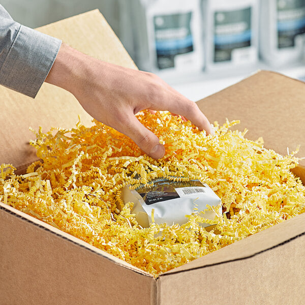 A hand reaching out to a box of Spring-Fill Canary Crinkle Cut Paper Shred.