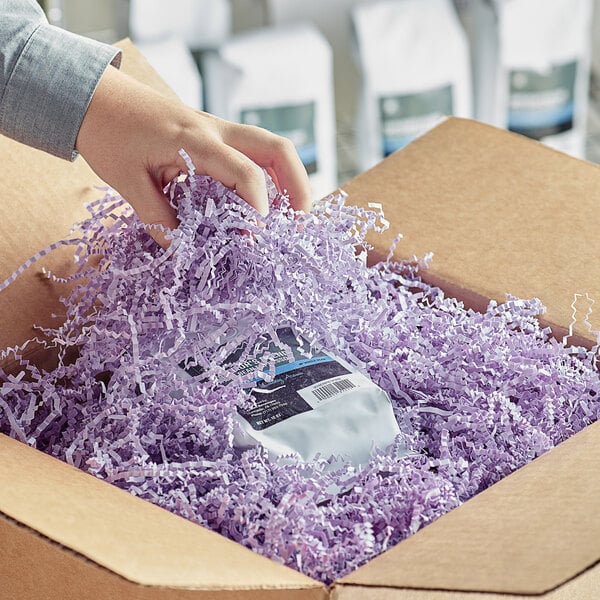 A hand holding a cardboard box filled with Spring-Fill Orchid Crinkle Cut paper shred in purple.