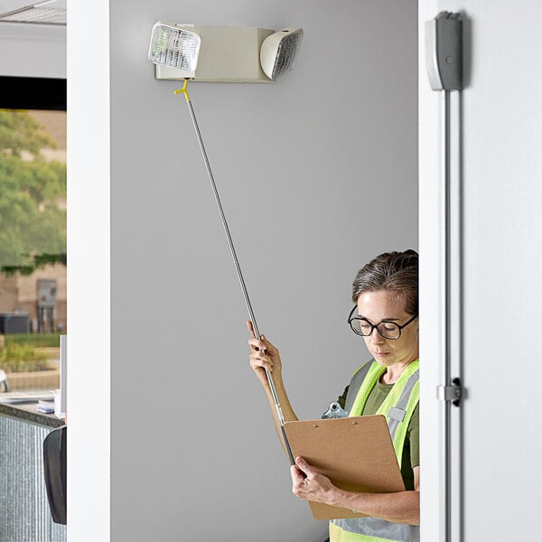 A woman using a CrewSafe TESS telescoping tool to test an emergency light.