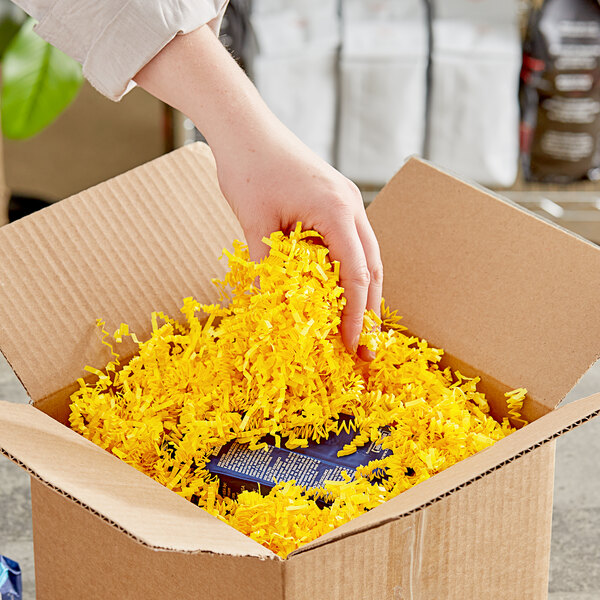 A hand holding a cardboard box with Spring-Fill yellow crinkle cut paper shred.