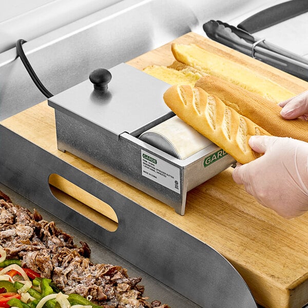 A person's hand holding a piece of bread using a Garde heated butter spreader.