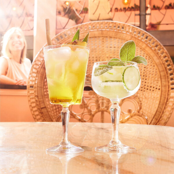 Two Arcoroc Monti cocktail glasses on a table filled with yellow drinks and ice.