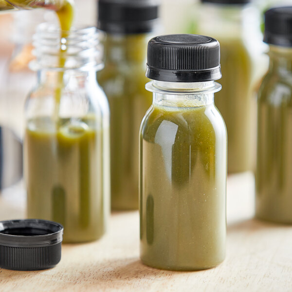 A 2 oz. round clear PET short energy bottle with black lid filled with green liquid on a counter.