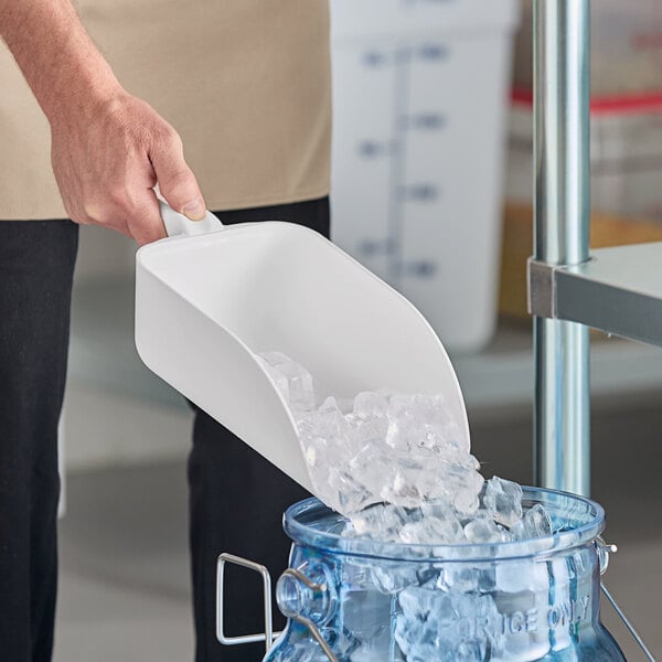 A person pouring ice from a white Vikan hand scoop into a container.
