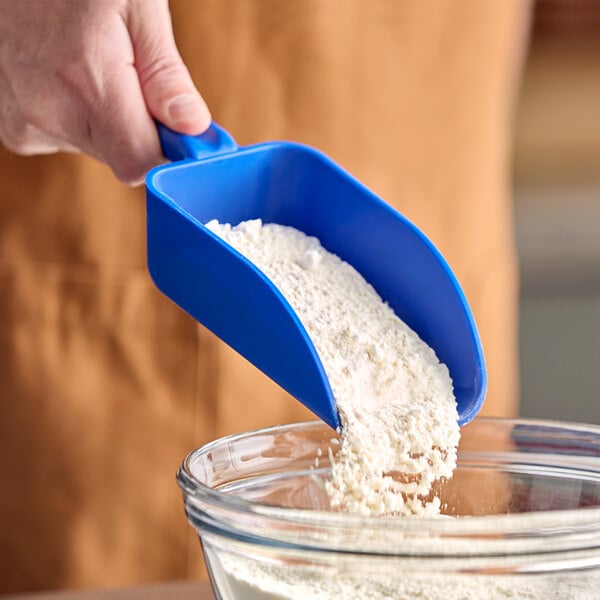 A hand holding a blue Vikan scoop pouring flour into a bowl.