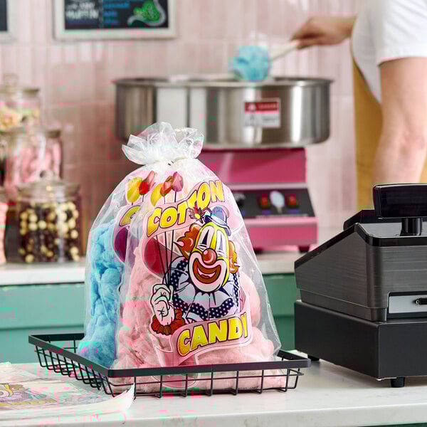 A clear plastic bag with a clown design filled with pink and blue cotton candy.