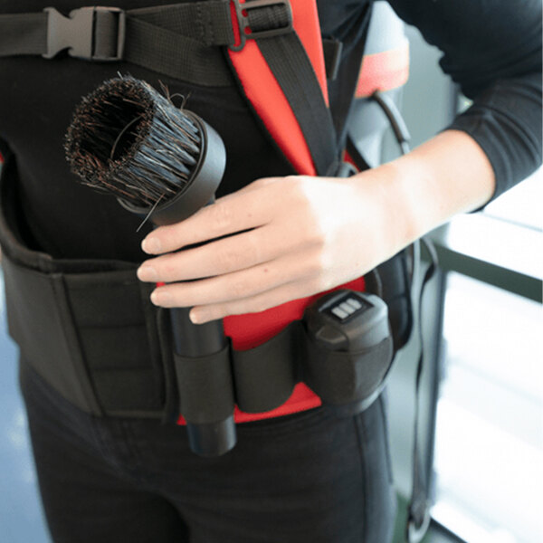A person wearing a tool belt using the NaceCare backpack vacuum's air driven brush kit.