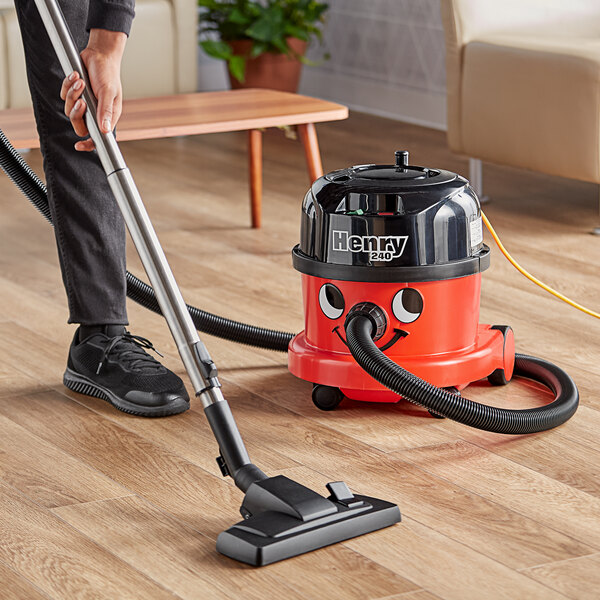 A person using a NaceCare canister vacuum to clean a wood floor.