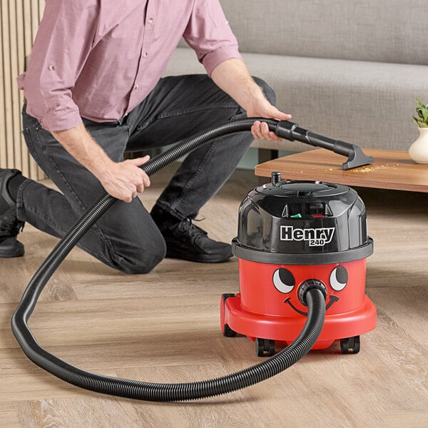 A man using a NaceCare canister vacuum with a hard floor kit to clean a floor.