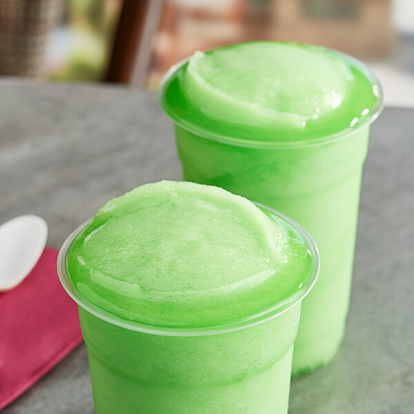 Two plastic cups of green Philadelphia Water Ice sitting on a table.