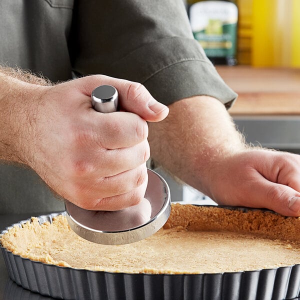 A person using a stainless steel meat tenderizer to press a pie crust.