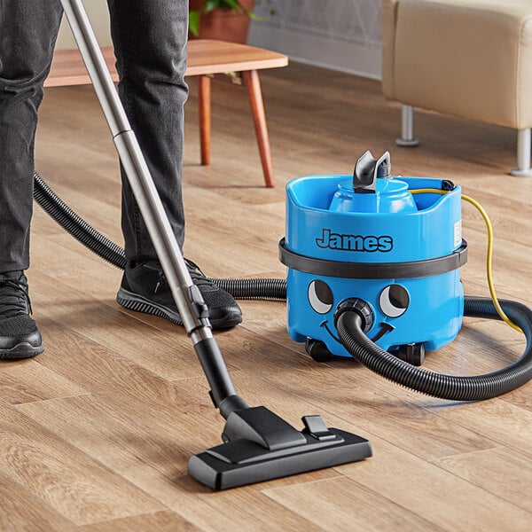 A man using a NaceCare canister vacuum to clean a hardwood floor in a professional kitchen.