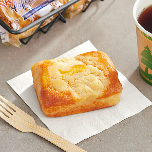 A Ne-Mo's Bakery box of Cream Cheese Coffee Cake on a napkin next to a cup of coffee.