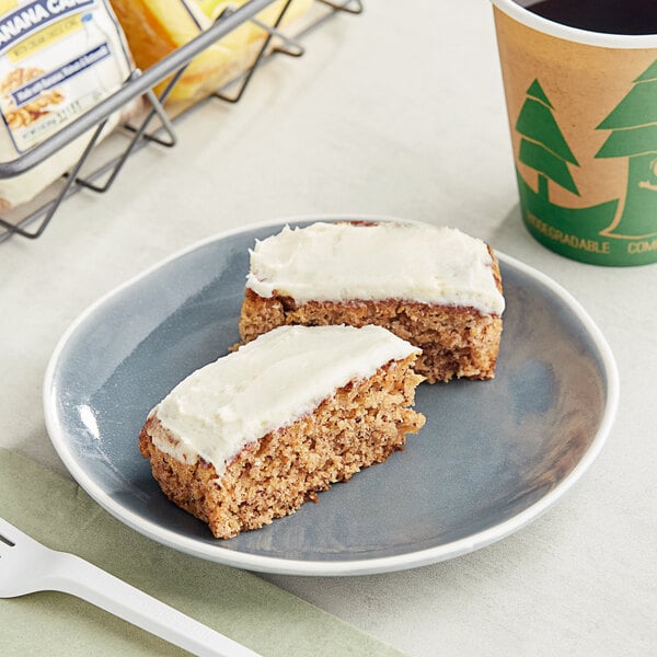 A plate with two Ne-Mo's Bakery banana cake squares with white frosting on a plate next to a cup of coffee.