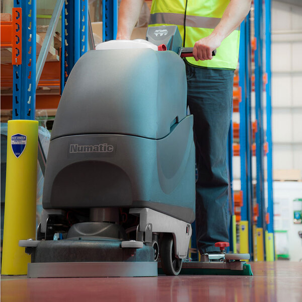 A person using a NaceCare cordless walk behind floor scrubber to clean a floor.