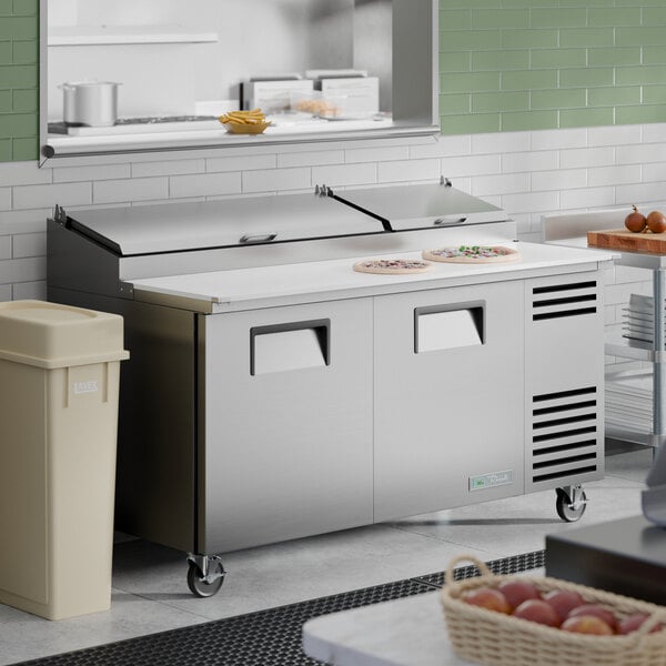 A stainless steel two-door refrigerated pizza prep table with a white cutting surface and closed top compartments.