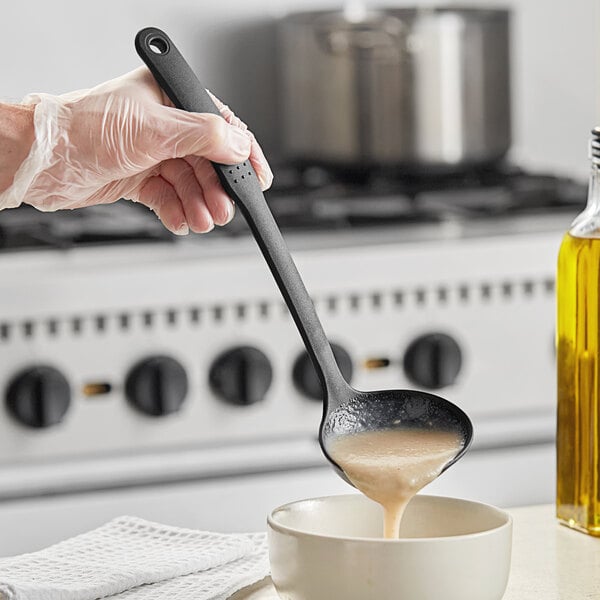 A hand holding a black Choice ladle over a bowl of liquid.