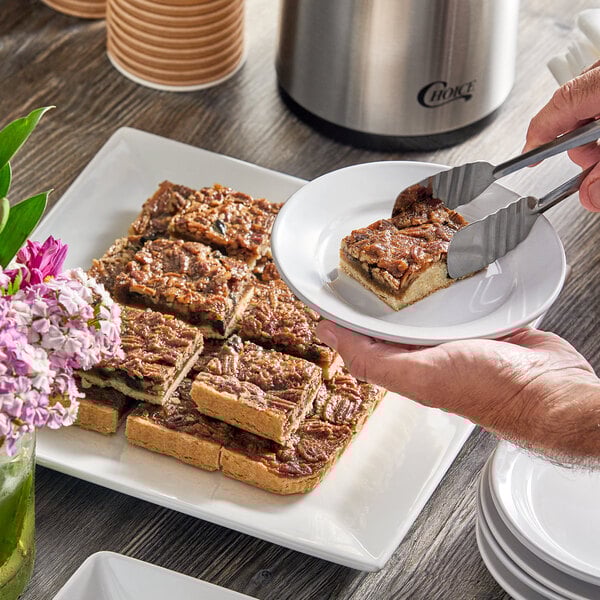 A person serving a Sweet Street Desserts Pecan Chocolate Chunk Dessert Bar on a plate.