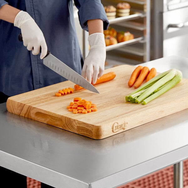 A person cutting carrots on a Choice wooden cutting board.