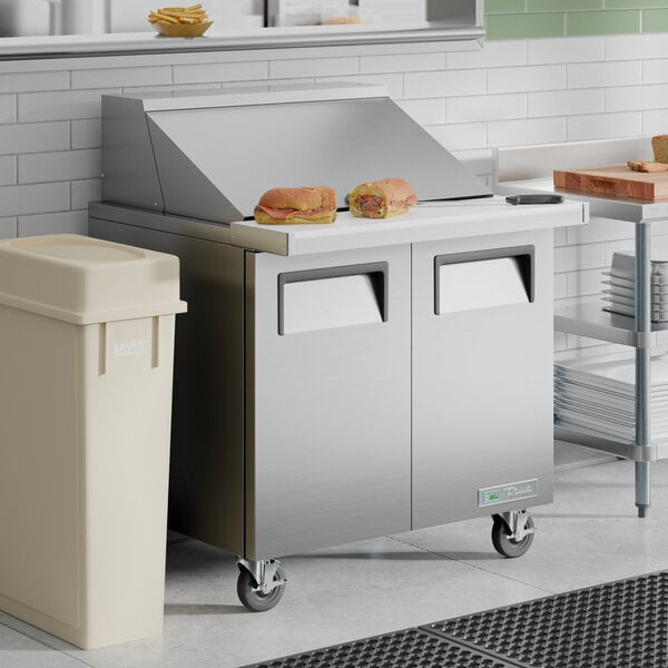 A stainless steel two-door mega top refrigerated sandwich prep table with a flat work surface and sandwiches on top.