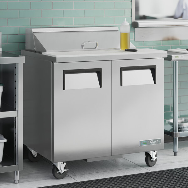 A stainless steel True refrigerated sandwich prep table in a commercial kitchen.