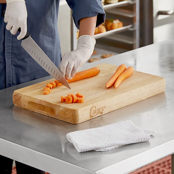 A person cutting a carrot on a Choice wooden cutting board.