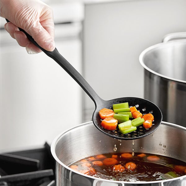 A hand holding a Choice black skimmer spoon over a pot of food.