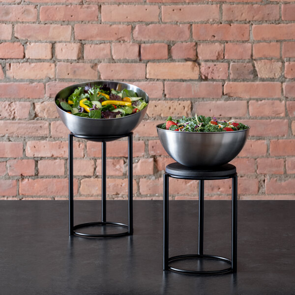 A stainless steel Arcoroc serving bowl filled with salad sits on a metal stand.