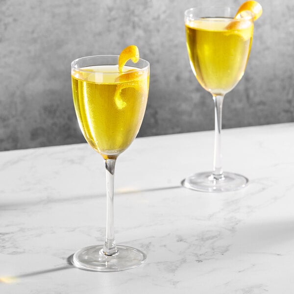 Two Della Luce Aurora Nick and Nora glasses filled with yellow liquid and a lemon peel.