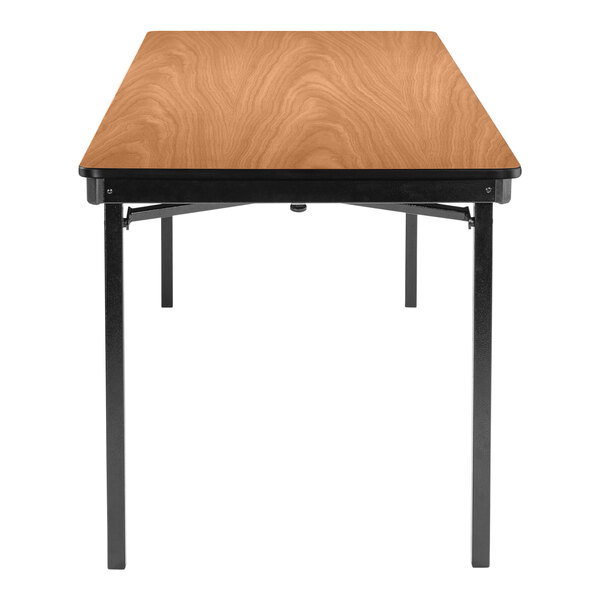 A National Public Seating rectangular Bannister Oak plywood folding table with black T-mold edge and legs.