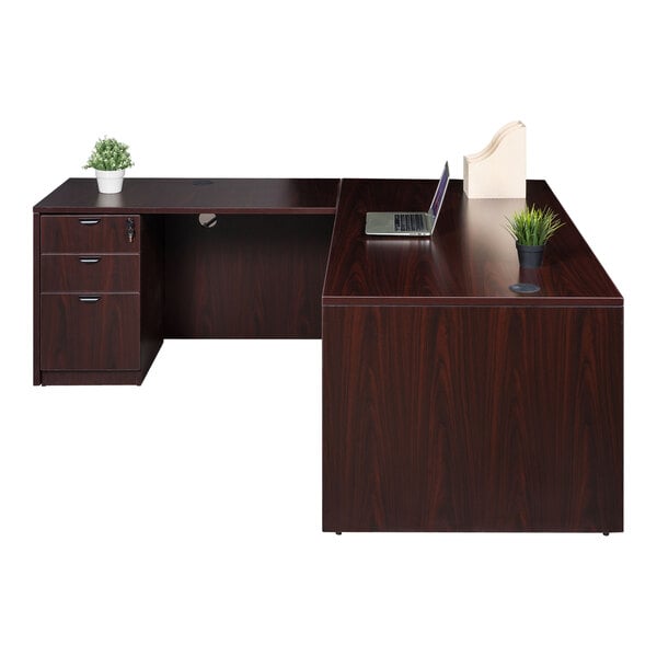 A Boss mahogany laminate desk with a laptop and potted plant on it.