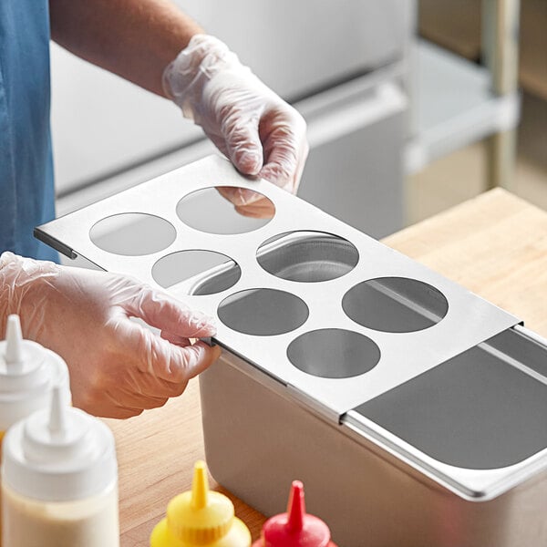 A person holding a metal container with seven holes in it over a tray of food.