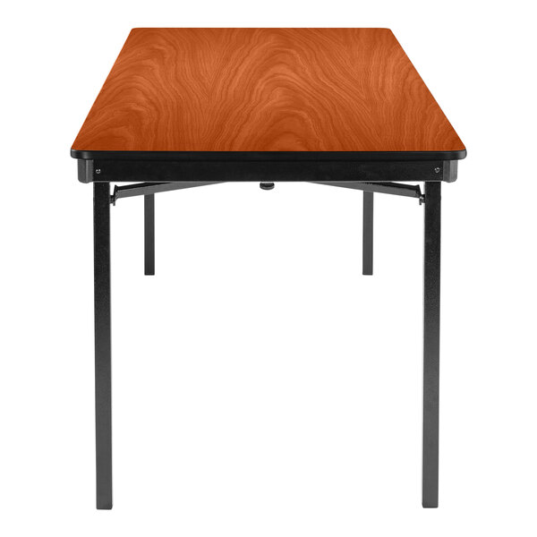 A National Public Seating rectangular wooden folding table with a Wild Cherry wood surface and black T-Mold edges.