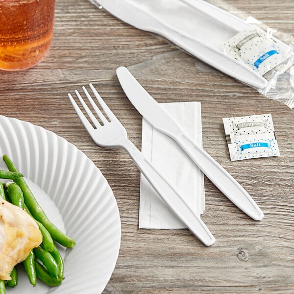 A white plate with green beans and a Choice white heavy weight plastic fork and knife on a napkin.