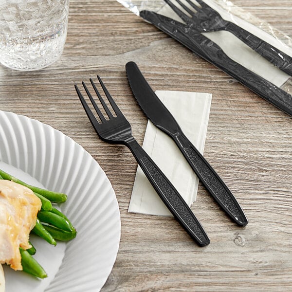 A Choice black heavy weight wrapped plastic fork and knife cutlery pack on a napkin.