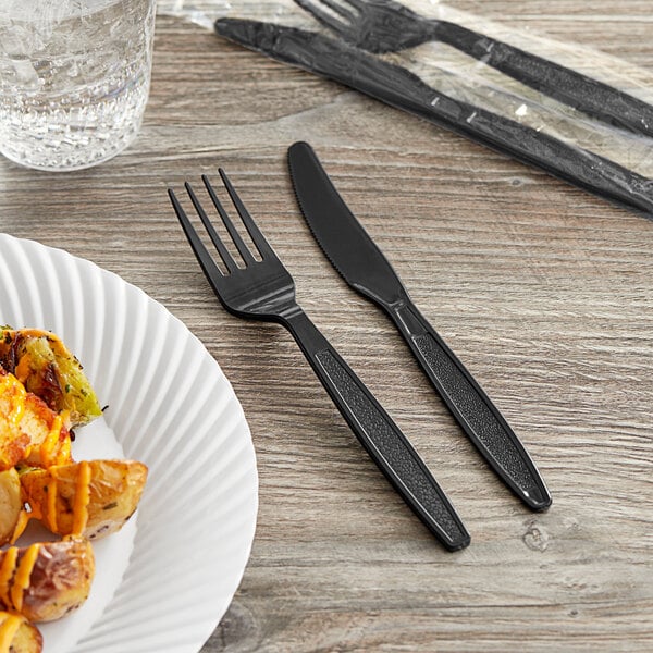 A wrapped black plastic fork and knife on a table with a plate of food