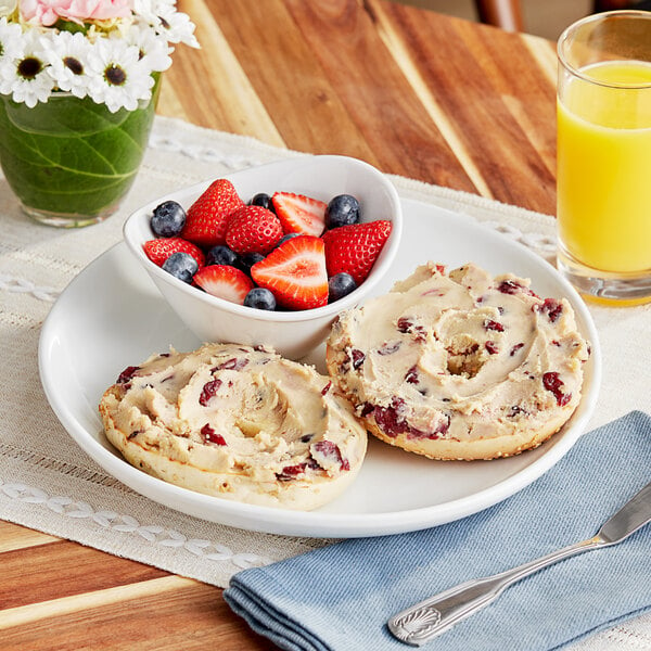 A plate with a bagel and Rind Cranberry Cream Cheese alongside a bowl of fruit.