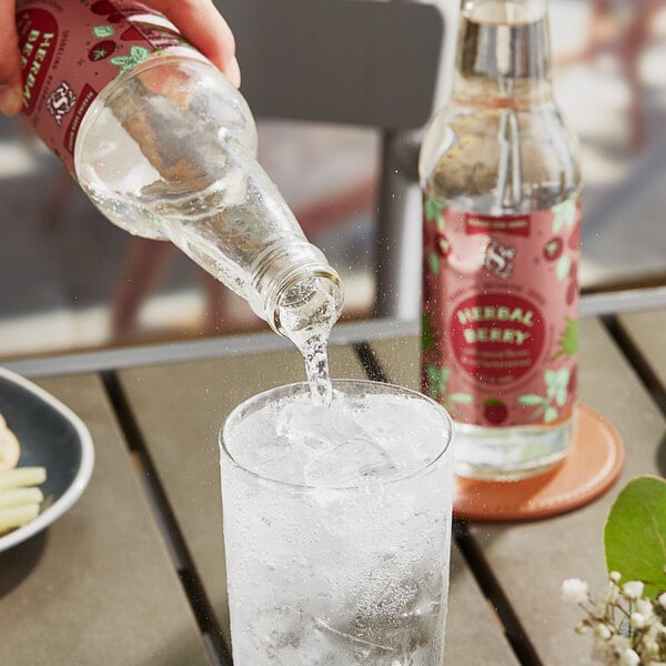 A person pouring Reading Soda Works Herbal Berry Soda into a glass with ice.