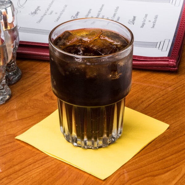 A glass of yellow liquid with ice on a sun yellow Hoffmaster cocktail napkin.