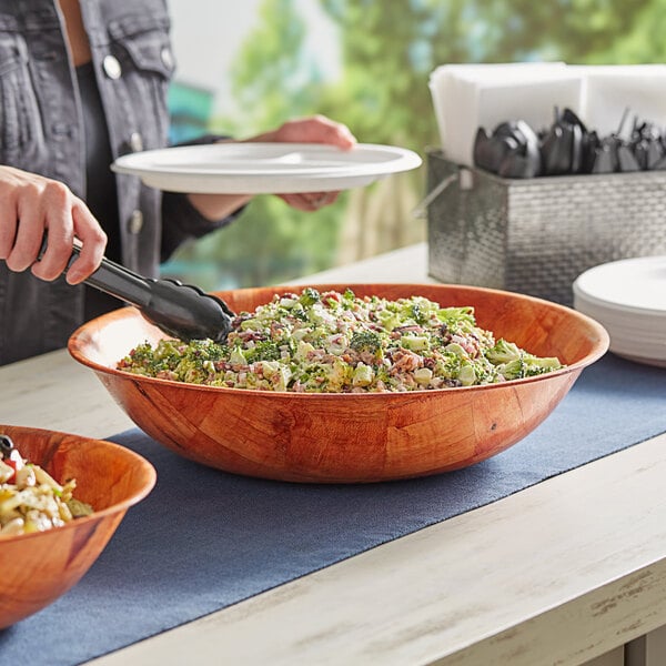 A woman serving salad in a Choice woven wood salad bowl at a salad bar.