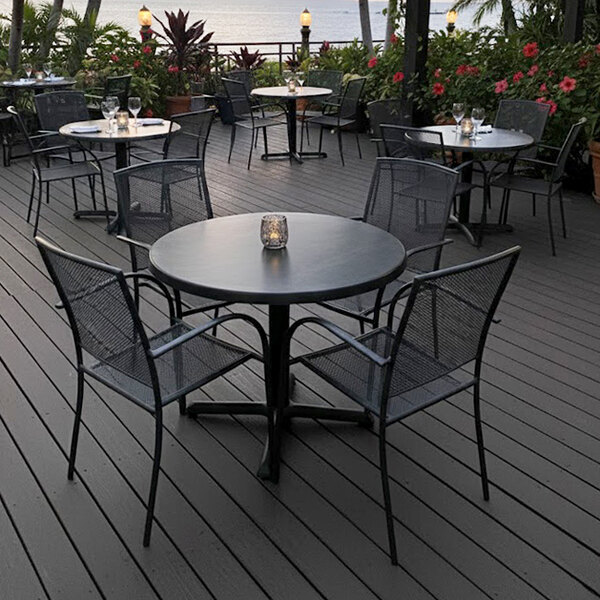 A black steel mesh outdoor chair with armrests and a wrinkle finish, placed around a round table on a patio.