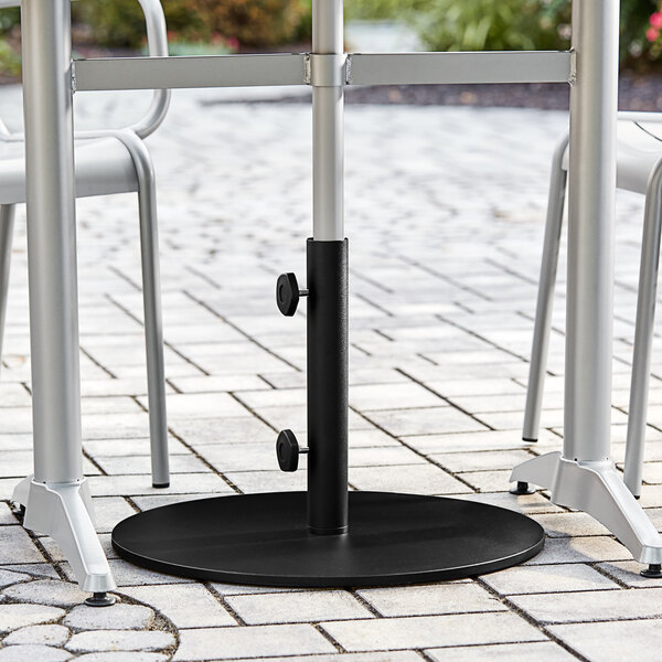 A black Lancaster Table & Seating round steel umbrella base on a brick patio.