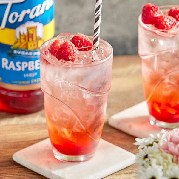 A glass of Torani Sugar-Free Raspberry flavoring syrup with a drink and straw.