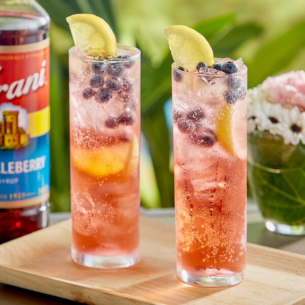 Two glasses of pink and blue drinks with Torani Huckleberry flavoring and lemon slices.