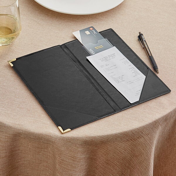 An American Metalcraft black leather check presenter with gold corners holding a bill, pen, and credit cards.